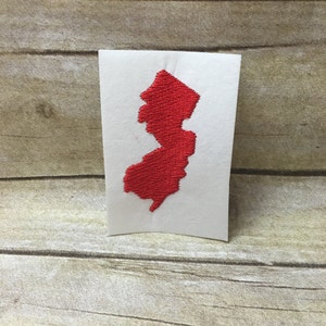 May include: Red embroidered outline of the state of New Jersey on a white background.