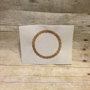 Puede incluir: Un cuadrado de tela blanca con un círculo dorado de cuerda bordado en el centro.