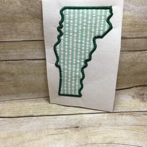 May include: Green outline of the state of Vermont with a light green and white gingham pattern inside.