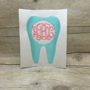 May include: A turquoise tooth-shaped embroidery design with a pink monogram in a circle in the centre.