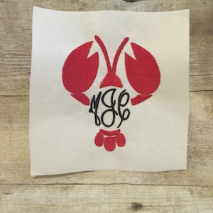 May include: Red embroidered lobster with a black monogram in the centre. The lobster is on a white background.
