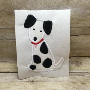 May include: A white and black embroidered patch of a Dalmatian dog wearing a red collar with a pink tag. The dog is sitting with its ears perked up.