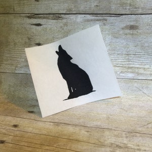 May include: A black silhouette of a wolf howling at the moon, embroidered on a white fabric patch.