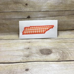 May include: A white card with an orange and white gingham pattern in the shape of the state of Tennessee.