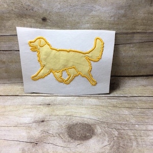 May include: A yellow embroidered outline of a golden retriever dog on a white background.