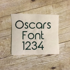 May include: A white piece of paper with the text "Oscars Font 1234" written in green embroidery thread.