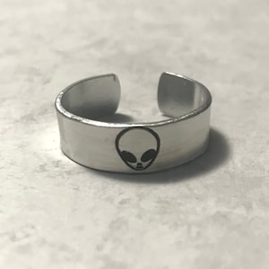 May include: A silver adjustable ring with an alien face design.