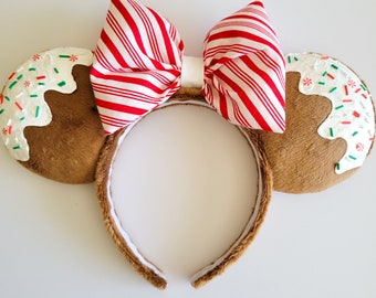 Puede incluir: Orejas de Minnie Mouse de color marrón con forma de pan de jengibre, con glaseado blanco y chispas rojas y verdes. Las orejas están coronadas con un lazo a rayas rojas y blancas.