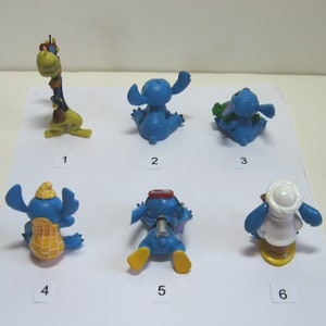 K&ouml;nnte beinhalten: Eine Sammlung von sechs kleinen, blauen Stitch-Figuren in verschiedenen Posen. Eine ist eine Giraffe, und die anderen tragen verschiedene Outfits oder halten Gegenst&auml;nde. Die Figuren sind mit 1 bis 6 nummeriert.