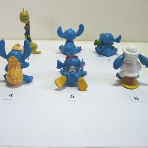 K&ouml;nnte beinhalten: Eine Sammlung von sechs blauen Stitch-Figuren in verschiedenen Posen. Eine tr&auml;gt eine Erdnussschale, eine andere h&auml;lt einen gr&uuml;nen Gegenstand und eine dritte tr&auml;gt ein wei&szlig;es Outfit. Die Figuren stehen auf einer wei&szlig;en Oberfl&auml;che.