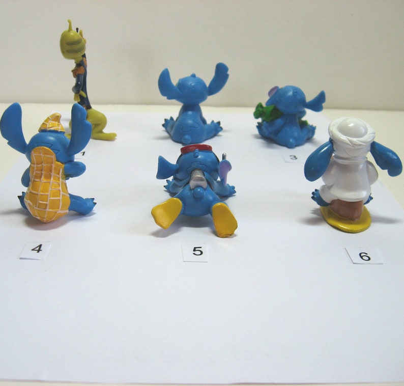 K&ouml;nnte beinhalten: Eine Sammlung von sechs blauen Stitch-Figuren in verschiedenen Posen. Eine tr&auml;gt eine Erdnussschale, eine andere h&auml;lt einen gr&uuml;nen Gegenstand und eine dritte tr&auml;gt ein wei&szlig;es Outfit. Die Figuren stehen auf einer wei&szlig;en Oberfl&auml;che.