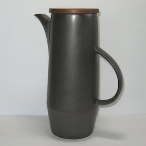 May include: A dark gray ceramic coffee pot with a wooden lid and a handle. The pot has a textured surface and a rounded body.