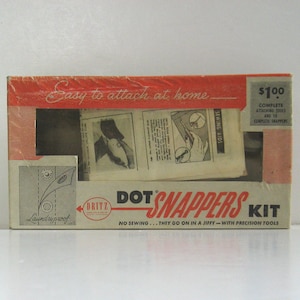 May include: A red and white box with the text "DOT SNAPPERS KIT" and "Easy to attach at home." The box contains a kit for attaching snaps to fabric. The kit includes tools and snaps. The box also says "Laundryproof" and "No sewing... they go on in a jiffy - with precision tools."