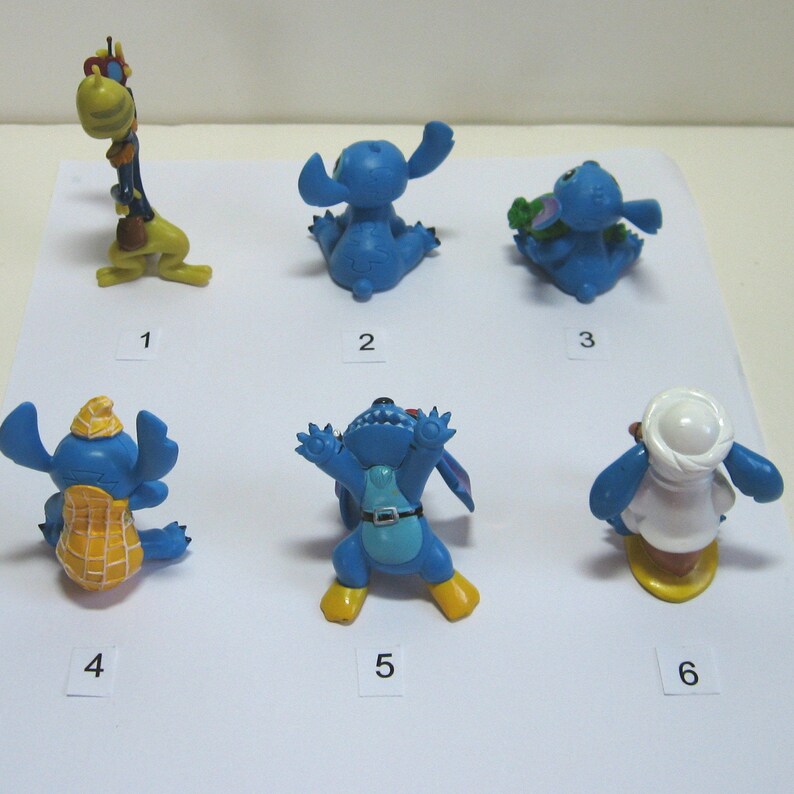 K&ouml;nnte beinhalten: Eine Sammlung von sechs kleinen, farbenfrohen Stitch-Figuren. Die Figuren sind in verschiedenen Posen und Outfits, darunter eine Giraffe, ein sitzender Stitch und Stitch mit Hut und Erdnussschale.