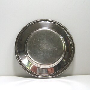 May include: A silver-plated round dish with a raised edge and a rope-like design around the rim.