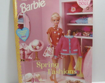 May include: A pink and white paper doll book featuring Barbie. The cover shows Barbie in a floral dress and a pink cardigan. The book is titled "Barbie Spring Fashions" and includes a "Paper Doll" label.