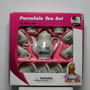 May include: A 13-piece porcelain tea set in a pink box. The set includes a teapot, cups, and saucers, all decorated with a blue and white duck design. The box reads "Porcelain Tea Set" and has a warning about choking hazards.