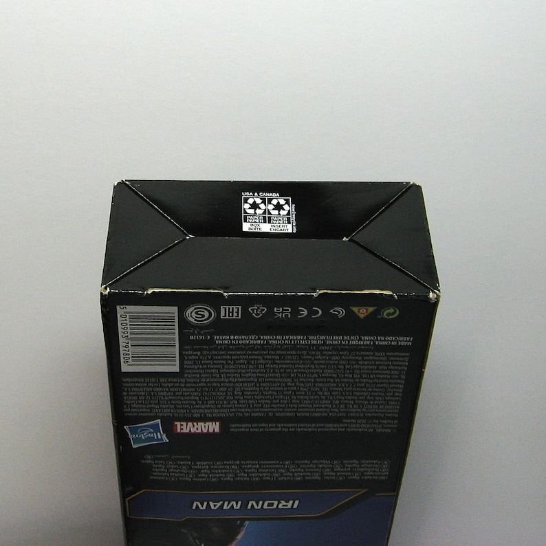 May include: A black cardboard box with the Marvel logo and the words "IRON MAN" in blue. The box has recycling symbols and text in multiple languages. The box is on a white background.