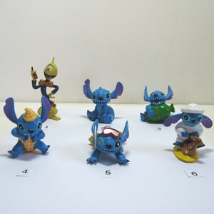 K&ouml;nnte beinhalten: Eine Sammlung von sechs Stitch-Figuren in verschiedenen Posen. Die Figuren sind haupts&auml;chlich blau mit gelben, wei&szlig;en und gr&uuml;nen Akzenten. Eine Figur tr&auml;gt eine Kochm&uuml;tze, eine andere eine Brille.