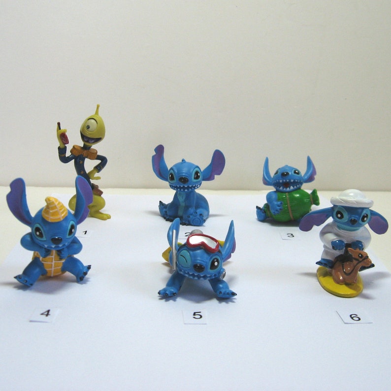 K&ouml;nnte beinhalten: Eine Sammlung von sechs Stitch-Figuren in verschiedenen Posen. Die Figuren sind haupts&auml;chlich blau mit gelben, wei&szlig;en und gr&uuml;nen Akzenten. Eine Figur tr&auml;gt eine Kochm&uuml;tze, eine andere eine Brille.