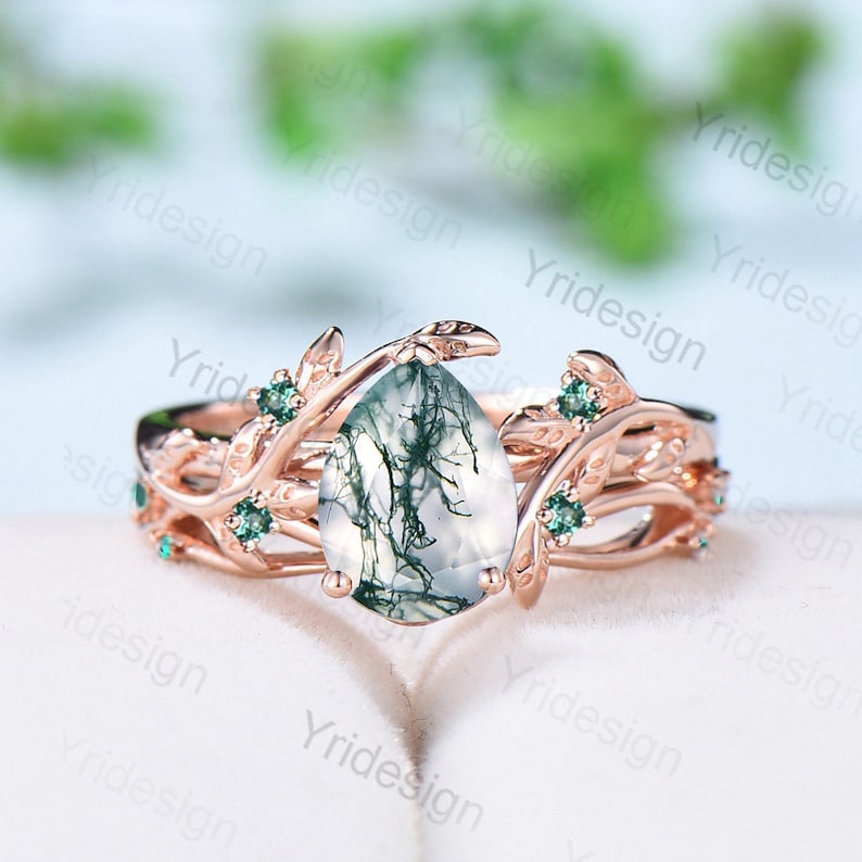 May include: A pear-shaped green agate gemstone ring with a rose gold band. The ring features a delicate, leafy design with small green gemstones set into the band.