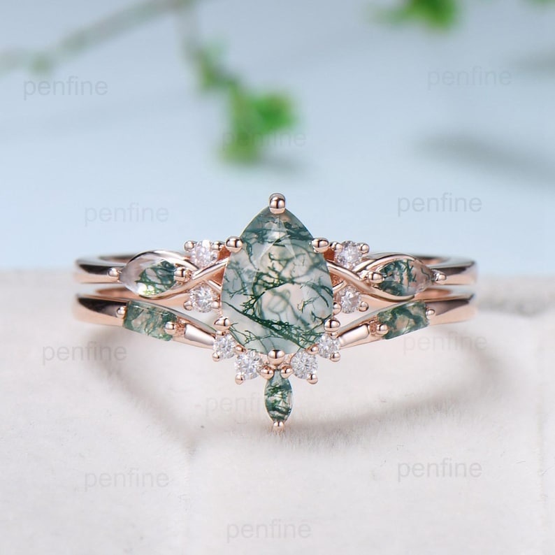 May include: A pear-shaped green moss agate engagement ring set with a rose gold band and a matching rose gold band with small diamonds and moss agate accents.
