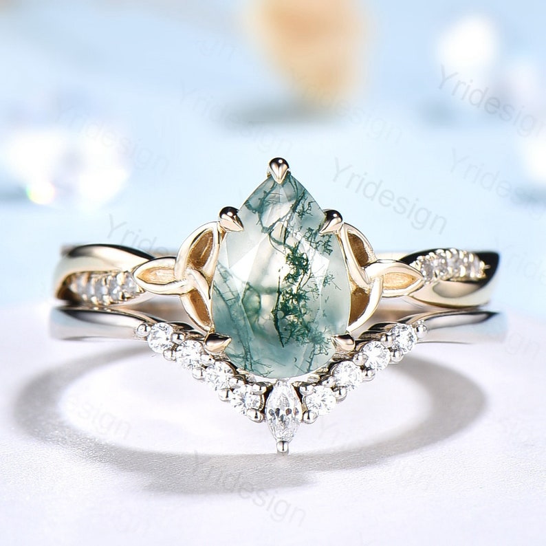May include: A pear-shaped green moss agate engagement ring set in a gold setting with a delicate, twisted band and a row of small diamonds. The ring is set on a white background.