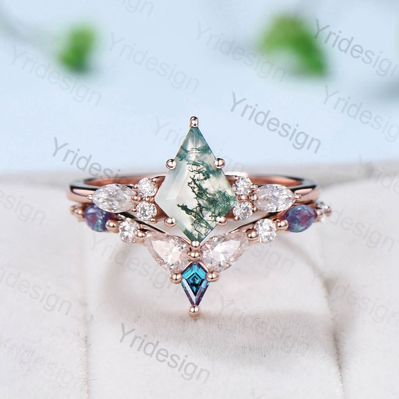 May include: A rose gold engagement ring set with a green moss agate center stone and a diamond halo. The band is adorned with smaller diamonds and two blue gemstones.