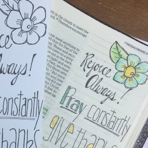 Könnte beinhalten: Ein weißes Lesezeichen mit schwarzer Tinte, auf dem "Freue dich immer! Bete ständig, danke für alles" steht. Das Lesezeichen ist mit einer schwarz-weißen Blume und Blättern verziert.