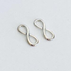 May include: Two silver infinity symbol charms. The charms are small and delicate, perfect for adding a touch of elegance to jewelry projects.