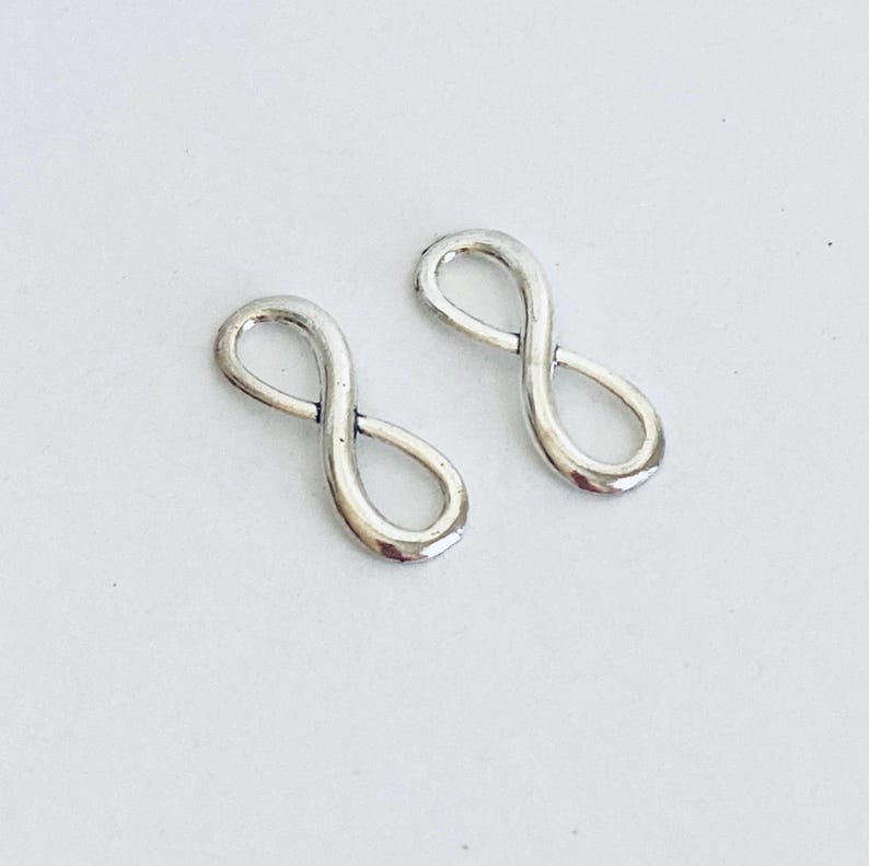 May include: Two silver infinity symbol charms. The charms are small and delicate, perfect for adding a touch of elegance to jewelry projects.