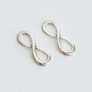 May include: Two silver infinity symbol charms. The charms are smooth and shiny.