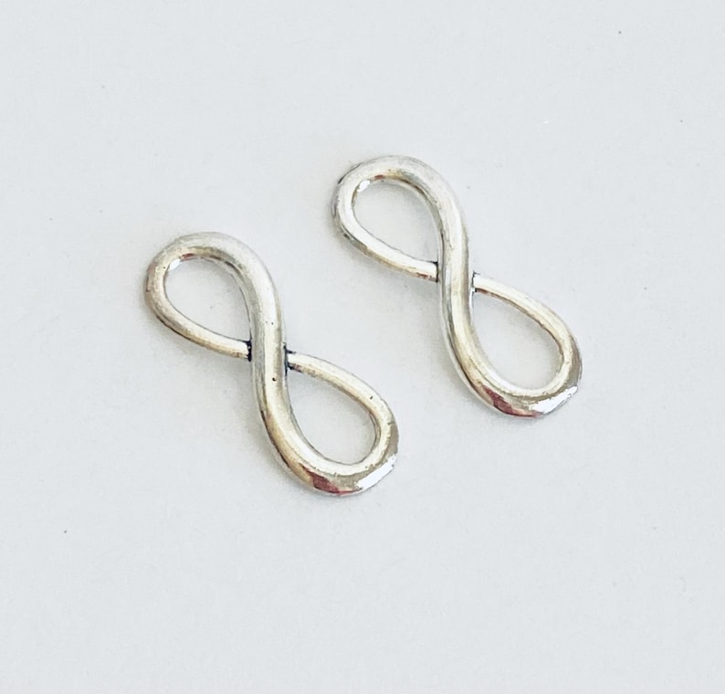 May include: Two silver infinity symbol charms. The charms are smooth and shiny.