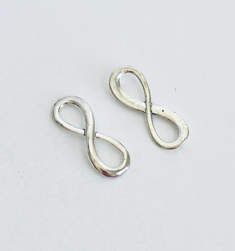 May include: Two silver infinity symbol charms. The charms are smooth and shiny.