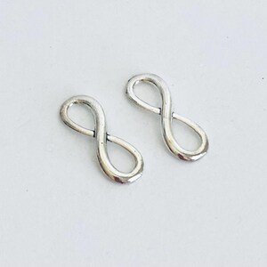 May include: Two silver infinity symbol charms. The charms are small and delicate, perfect for adding a touch of elegance to jewelry projects.