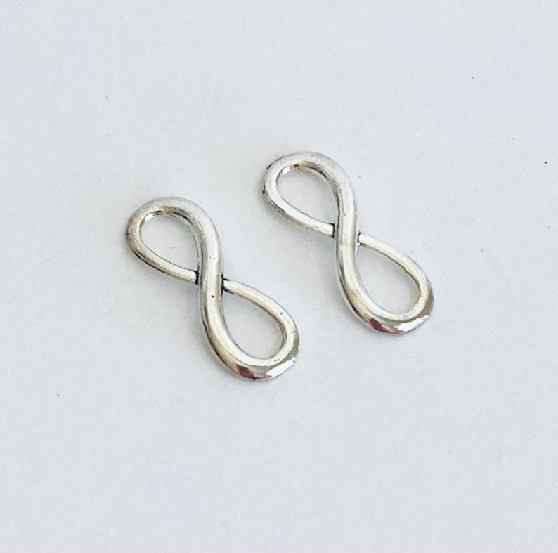 May include: Two silver infinity symbol charms. The charms are small and delicate, perfect for adding a touch of elegance to jewelry projects.