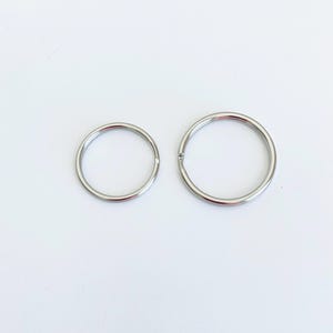 May include: Two silver key rings of different sizes. The larger ring is about 1 inch in diameter, and the smaller ring is about 3/4 inch in diameter.
