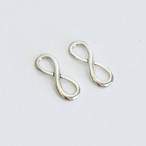 May include: Two silver infinity symbol charms. The charms are smooth and shiny.