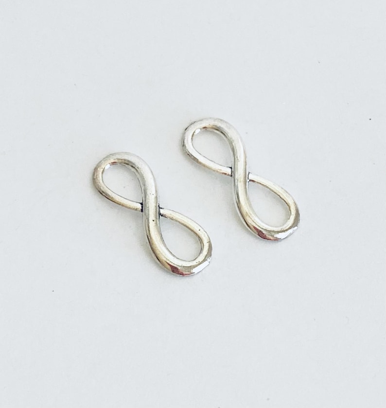 May include: Two silver infinity symbol charms. The charms are smooth and shiny.