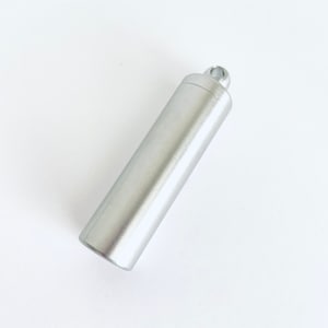 May include: A silver metal container with a loop at the top. The container is cylindrical and has a brushed finish.