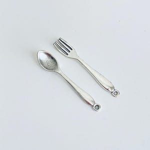 May include: A silver spoon and fork with a ring at the end of each handle.