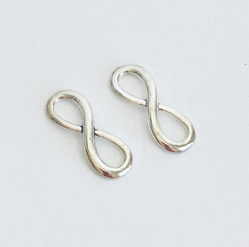 May include: Two silver infinity symbol charms. The charms are smooth and have a shiny finish.