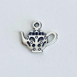 May include: Silver charm in the shape of a teapot with an intricate design. The teapot has a round body with a spout and a handle.