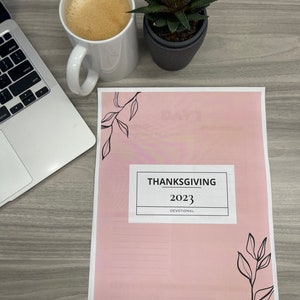 May include: A pink printable Thanksgiving devotional booklet with the title "Thanksgiving 2023 Devotional" and a simple black leaf design.