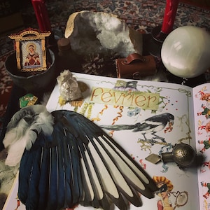 以下が含まれることがあります： 青い羽根と白い羽根のついた青いと白いカササギの羽、水晶、小さな木製の箱、宗教的な画像が入った小さな木製の額縁、表紙に「Fevrier」と書かれた本