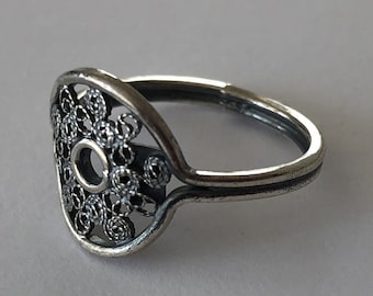 May include: A silver ring featuring a delicate filigree design. The ring has a round opening in the centre of the design.