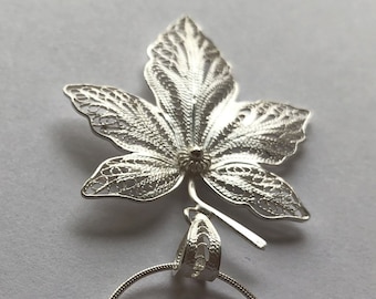 Op de afbeelding: Een zilveren filigraan hanger in de vorm van een esdoornblad, hangend aan een zilveren ketting.