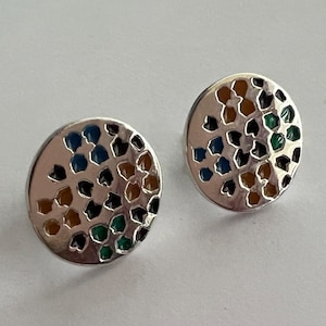 Può includere: Un paio di orecchini a bottone argentati. Ogni orecchino presenta un design circolare con un motivo di forme colorate in blu, marrone, verde e nero. Gli orecchini hanno una finitura lucida e uno stile semplice e moderno.