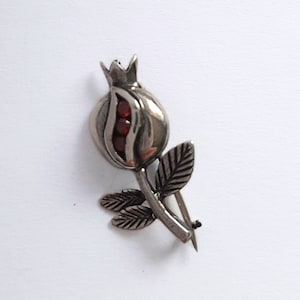 May include: A silver brooch in the shape of a pomegranate flower with red gemstone accents.