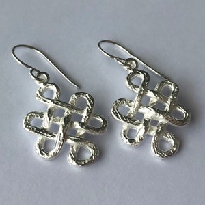 May include: A pair of silver earrings with a knotted design. The earrings are made of a textured metal and have a simple, elegant style.
